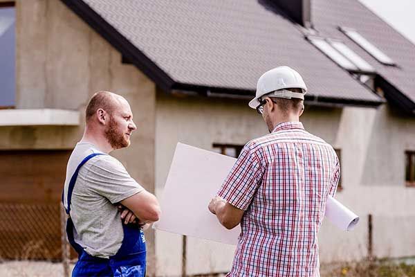 Two specialists reviewing plans outside a house